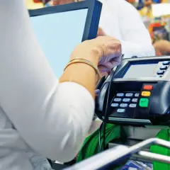 Kobieta płaci kartą przy terminalu. Na ekranie widoczny jest raport kasowy.