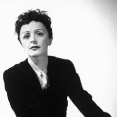 Edith Piaf, ikona francuskiej piosenki, w czarnym żakiecie i z charakterystyczną fryzurą. Jej piosenki wciąż poruszają serca.