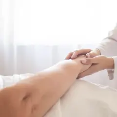 Delikatne dotknięcie dłoni pielęgniarki na ramieniu pacjenta, wskazujące na troskę i pomoc w procesie, jak wyleczyć odleżyny.