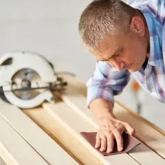 Stolarz szlifuje deski, przygotowując je do cięcia wzdłuż. Obok leży piła tarczowa.