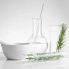 Laboratorio con mortaio, provette e becher contenenti rosmarino e liquido limpido, forse benzyl alcohol per estrarre essenze naturali.