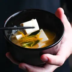 A chopstick lifts a cube of tofu from a bowl of miso soup, showcasing simple yet delicious tofu recipes.