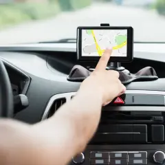 Dłoń dotyka ekranu nawigacji samochodowej, która pokazuje mapę. To najlepsza nawigacja samochodowa na telefon, która ułatwia podróż.
