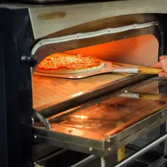 Une main glisse une pizza dans un four à pizza professionnel. La chaleur intense du four est visible, promettant une cuisson parfaite.