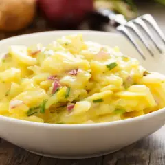 Schüssel mit cremigem Kartoffelsalat, garniert mit Schnittlauch und roten Zwiebeln. Perfekt für 7 Tassen Salat.
