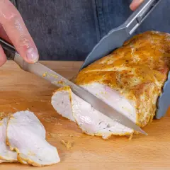 Ein saftiger Schweinelachs wird auf einem Holzbrett in Scheiben geschnitten. Die goldbraune Kruste und das zarte Fleisch sind gut sichtbar.