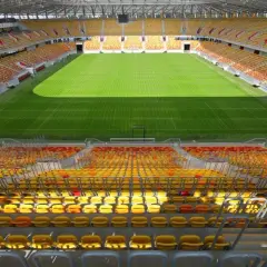 Pusta trybuna stadionu Jagiellonii, z żółtymi i czerwonymi siedzeniami, czeka na kibiców. Pojemność stadionu robi wrażenie.