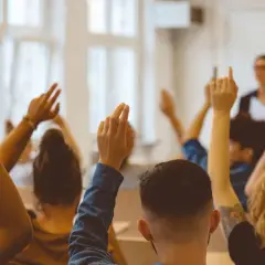 Schüler heben die Hände, um Fragen zu stellen. Ein achtsamkeit lehrer im Hintergrund beobachtet die Klasse.