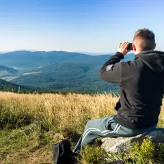 Mężczyzna siedzi na skale, robiąc zdjęcie krajobrazu telefonem z aparatem szerokokątnym.