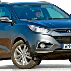 Ciemnoszary Hyundai Tucson, jeden z popularnych koreańskich samochodów, z kierowcą w czerwonej czapce za kierownicą.