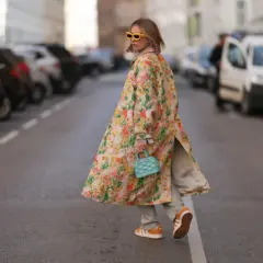 Kobieta w kwiecistym płaszczu i pomarańczowych sneakersach idzie ulicą.