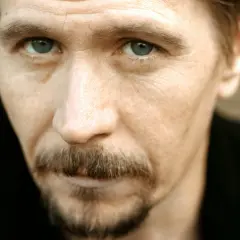 Młody Gary Oldman z przenikliwym spojrzeniem i charakterystycznym wąsikiem.