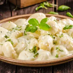 Pyszne gnocchi z kurczakiem w kremowym sosie, udekorowane bazylią i parmezanem, na drewnianym stole.