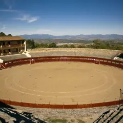 La plaza de toros El Castañar, con su arena de arena y gradas de piedra, se alza majestuosa ante un paisaje montañoso.
