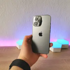 Dłoń trzyma szary iPhone 13 Pro z potrójnym aparatem. Wymiary telefonu idealnie pasują do dłoni.