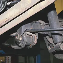 Mechanik pracuje przy wahaczu w samochodzie, używając narzędzia do regulacji.