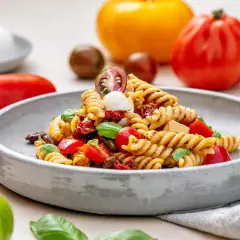Ein köstlicher italienischer Nudelsalat mit Fusilli, Tomaten, Mozzarella und Basilikum, serviert auf einem grauen Teller.