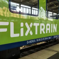 Zielony pociąg FlixTrain z białym logo na tle torów kolejowych.
