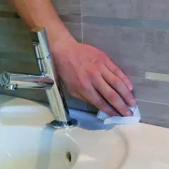 Dłoń wyciera brzeg wanny, przygotowując go do tego, jak polozyc silikon w lazience.