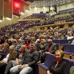Widownia filharmonii pełna elegancko ubranych osób. Zastanawiasz się, jak się ubrać do filharmonii? Tutaj widzisz inspiracje: klasyczne stroje, garnitury, sukienki.