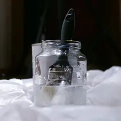 Pędzel zanurzony w słoiku z płynem, prawdopodobnie terpentyną balsamiczną, gotowy do czyszczenia.