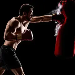 Boxer training to strengthen his chin for boxing, punching a red heavy bag with force.