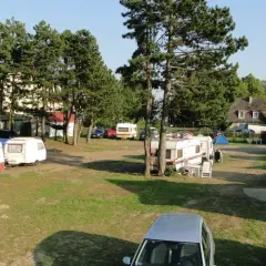 Wypoczynek na kempingu nad Bałtykiem w Mielnie. Przyczepy kempingowe i samochody na trawiastym terenie, otoczone drzewami.
