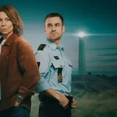 Två poliser står på en kulle med vit sand. I bakgrunden syns ett fyrhus vid havet.