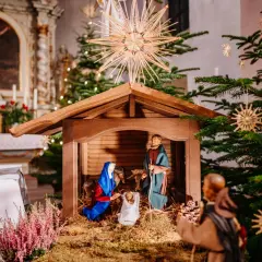 Krippe in einer Kirche, die zeigt, was ist Weihnachten: Maria, Josef und das Jesuskind. Weihnachtsbäume und Kerzen schmücken den Altarraum.