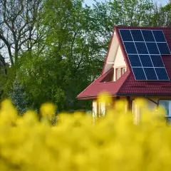 Dom z panelami fotowoltaicznymi na dachu, otoczony kwitnącym rzepakiem. Dobór instalacji fotowoltaicznej to krok w stronę ekologii.