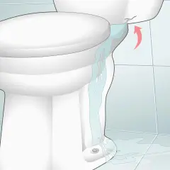Water is leaking from a cracked toilet tank, causing low water in the toilet bowl and a puddle on the floor.