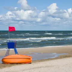 Ratownik z czerwoną flagą i łodzią ratunkową na plaży nad wzburzonym Bałtykiem.