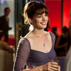 Uśmiechnięta Anne Hathaway w fioletowej sukience, trzymająca drinka. Scena z jednego z jej filmów.