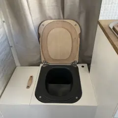WC de camping aménagé avec abattant en bois et cuvette noire.