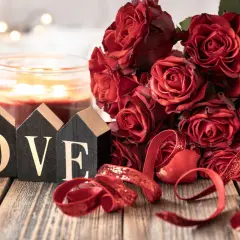 Drewniane domki z napisem LOVE, bukiet czerwonych róż i świeca tworzą romantyczną atmosferę na 11 rocznicę ślubu.
