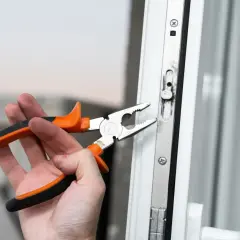 Dłoń z kombinerkami reguluje mechanizm okna, przygotowując je do trybu zimowego.
