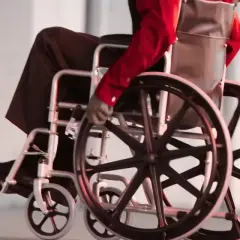 Osoba na wózku inwalidzkim w czerwonej koszuli i czarnych spodniach porusza się po chodniku.