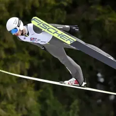 Skoczek narciarski w locie na tle lasu.