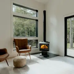 Un poêle à granule appartement, avec deux fauteuils en cuir marron et une vue sur la forêt.