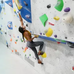 Eine Frau klettert an einer Boulderwand. Das zeigt, was ist bouldern: eine Herausforderung für Kraft und Geschicklichkeit.