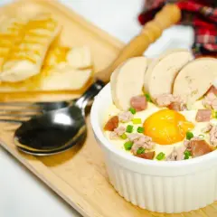 Un œuf cocotte bain-marie, garni de saucisse et de viande hachée, servi avec des bâtonnets de pain grillé.