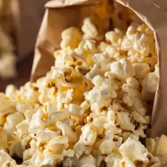 Góra popcornu wysypuje się z papierowej torby. Czy popcorn jest zdrowy? To zależy od sposobu przygotowania.