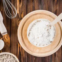Mąka orkiszowa, podobnie jak pszenna, zawiera gluten. Na zdjęciu widać składniki do pieczenia: mąkę, chleb, ziarna słonecznika, wałek i trzepaczkę.