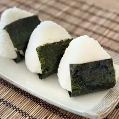 Trzy pyszne onigiri, czyli japońskie kulki ryżowe zawinięte w nori, leżą na talerzu.