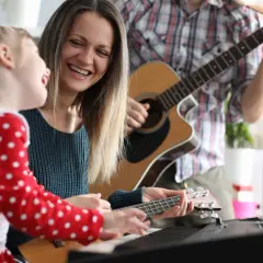Rodzina gra na instrumentach, tworząc piosenki o mamie. Radość i muzyka wypełniają dom.