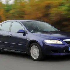 Granatowa Mazda 6 GG jedzie po drodze, za nią rozmyty krajobraz jesiennych drzew.