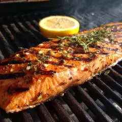 En saftig grillad laxsida med örter och en citronskiva på grillen. Röken stiger och lockar till en härlig måltid.