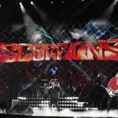 Zespół Scorpions na scenie z dużym logo zespołu i efektami świetlnymi.