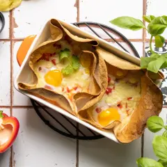 Pyszna tortilla na ciepło z piekarnika z jajkiem i serem, ozdobiona kolendrą. Obok papryka i bazylia.