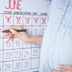 Ciężarna kobieta zaznacza dni na kalendarzu, odliczając, ile tygodni trwa ciąża.
